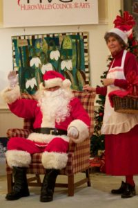 Santa Claus waving with Mrs. Claus at arts event.