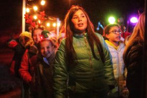 Children singing in festive holiday attire at night.