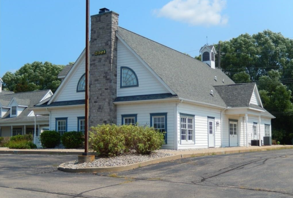 White building with stone chimney, surrounded by trees.