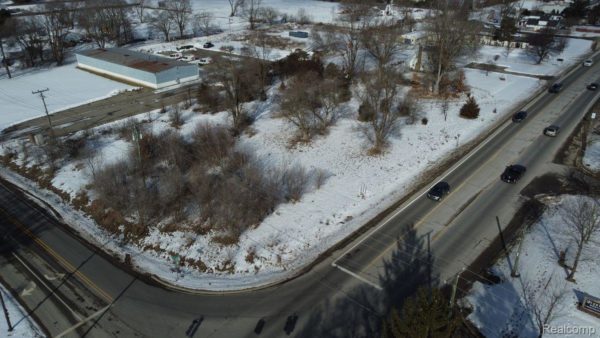 Snow-covered road intersection with cars and buildings.