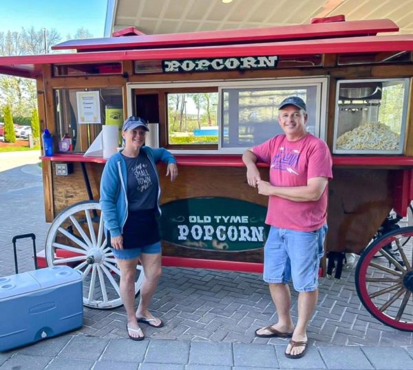 People at vintage popcorn stand outdoors.