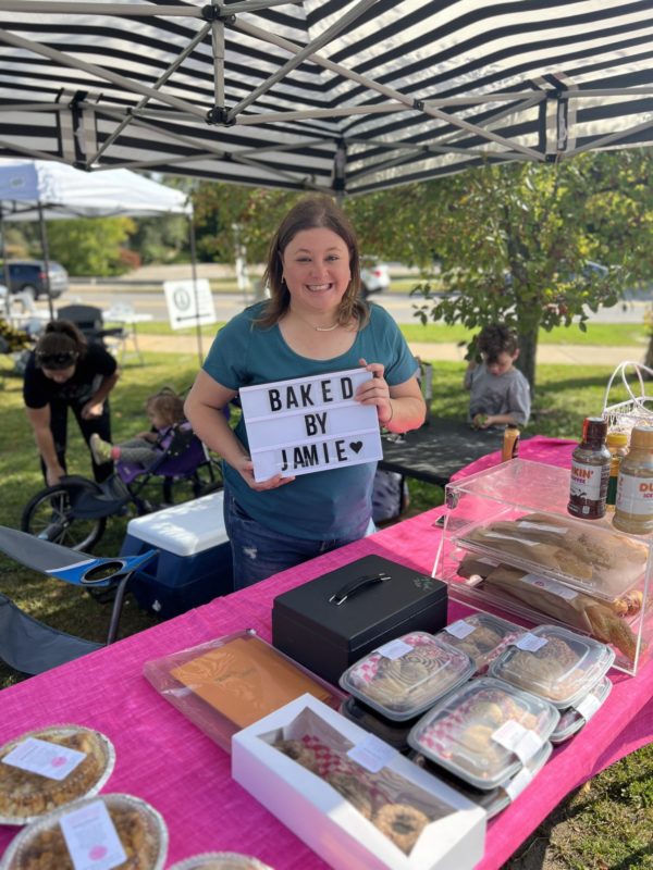 Woman selling baked goods at outdoor market stand.