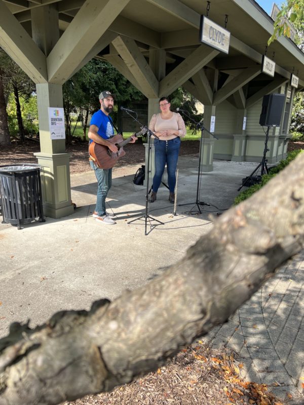 Two musicians performing outdoors with microphones and guitar.