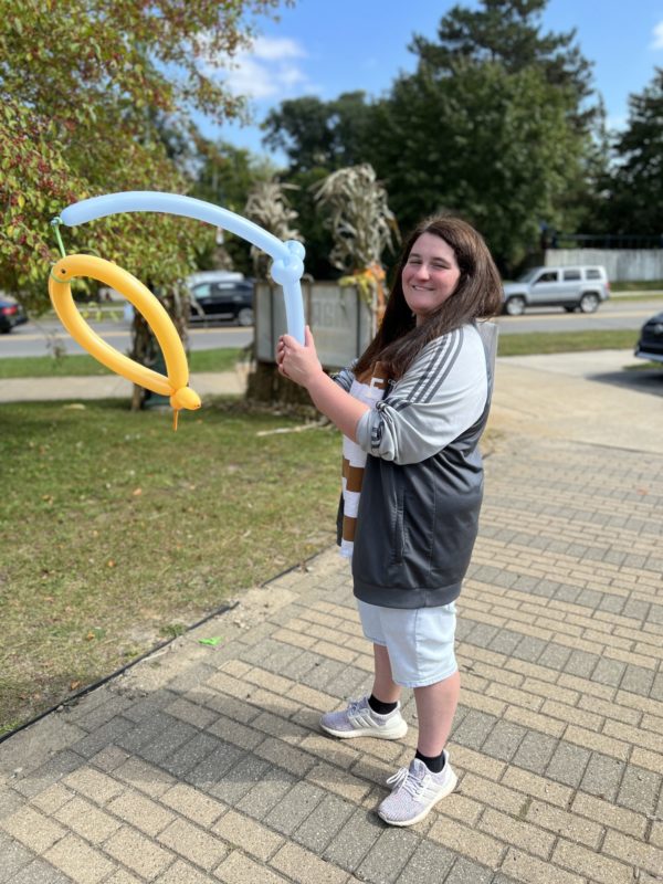 Person holding balloon sculpture outdoors, smiling in daylight.